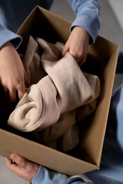 Clothing being folded into a cardboard donation box