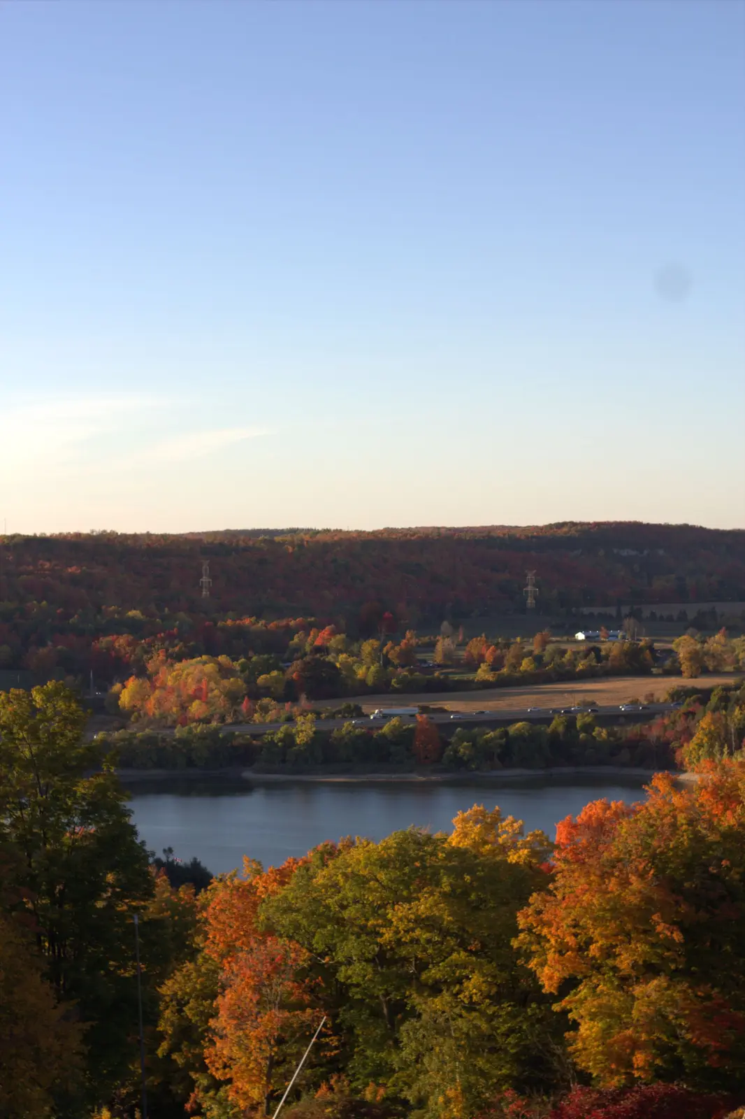 Autumn-coloured trees above a small lake, with rolling wooded hills behind, in Halton Hills, Ontario.