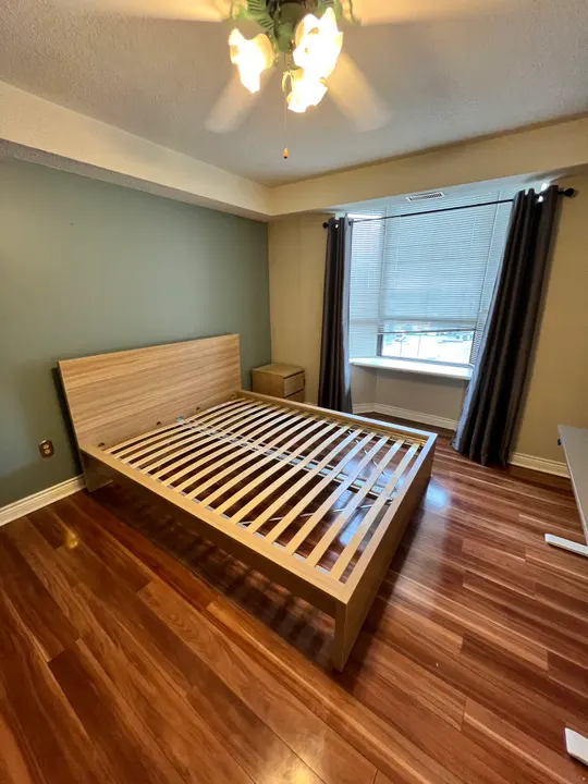 An assembled wooden bed frame with exposed support slats in a bedroom