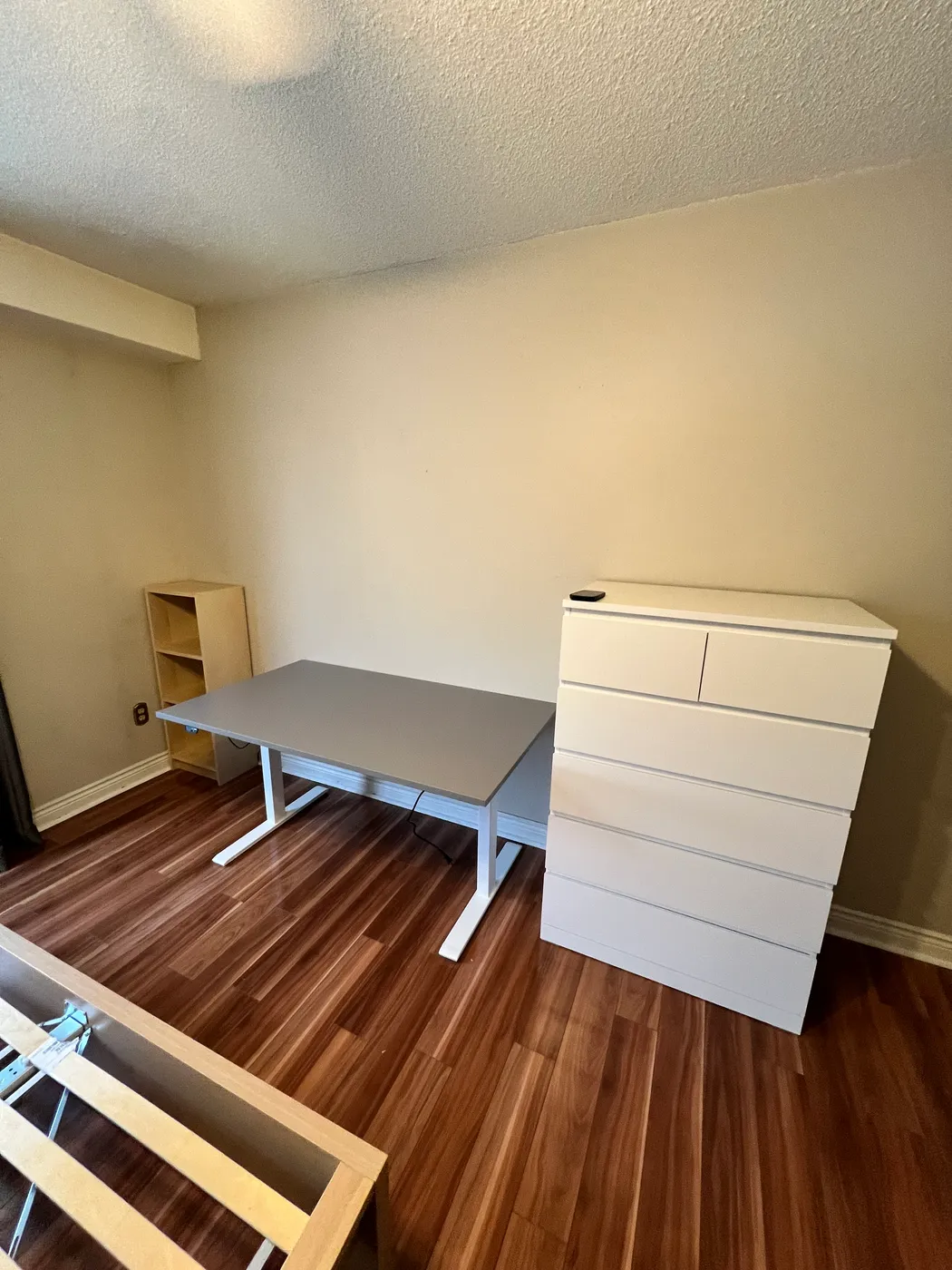 An assembled desk and white chest of drawers beside shelving in a room